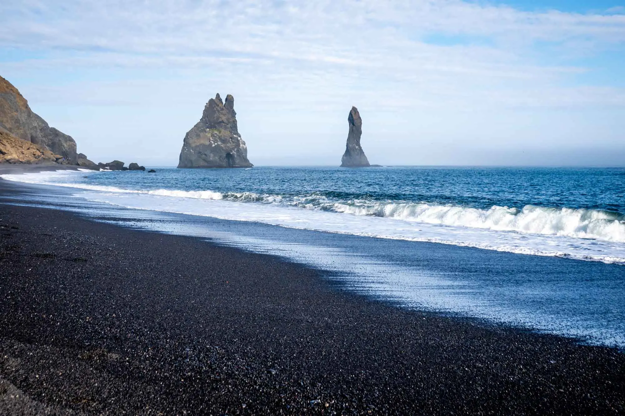 Rock formations in the ocean right off a black sand beach
