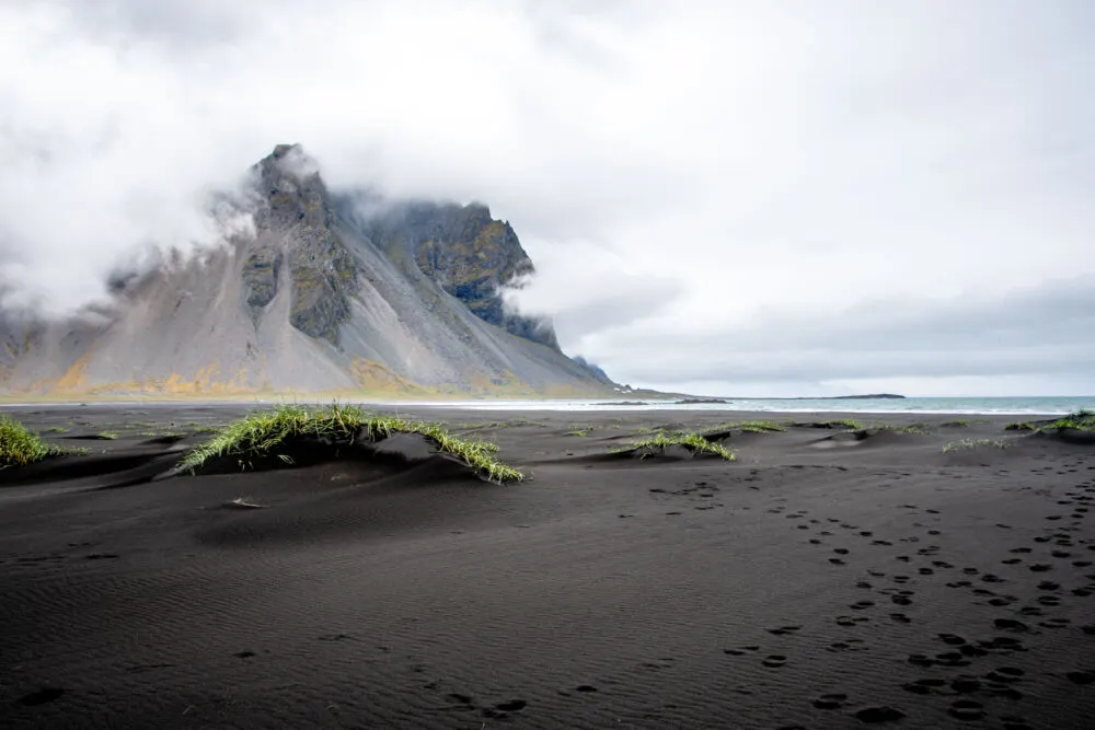 Mountain shrouded in clouds arising from a black sand beach