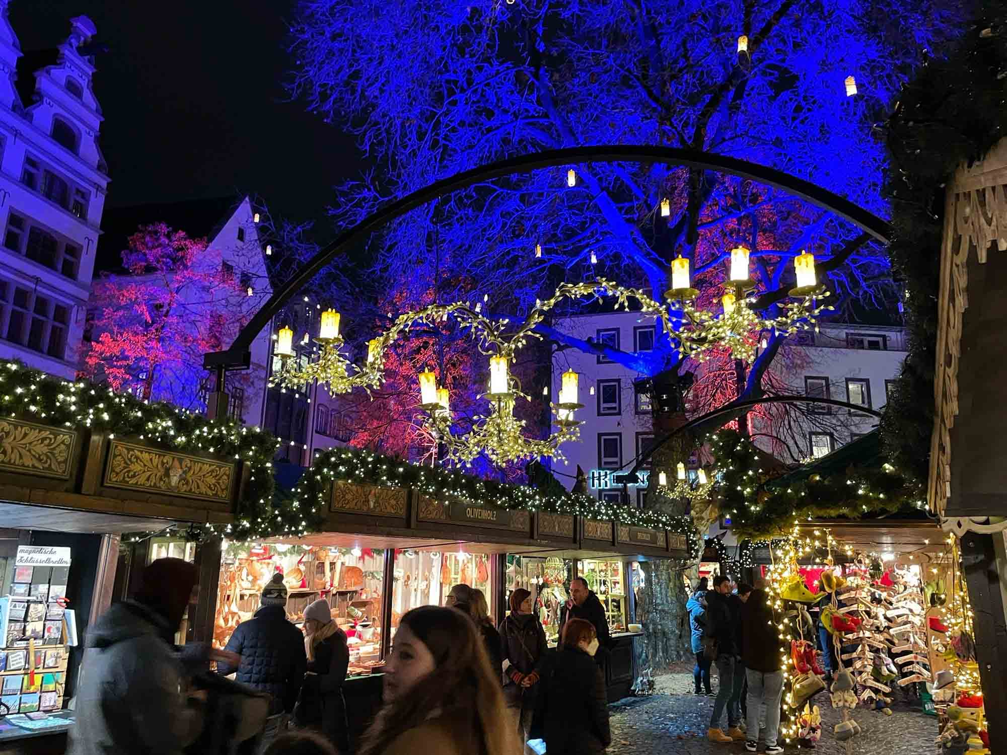 People shopping at a Christmas market at night beneath lights and candle chandeliers