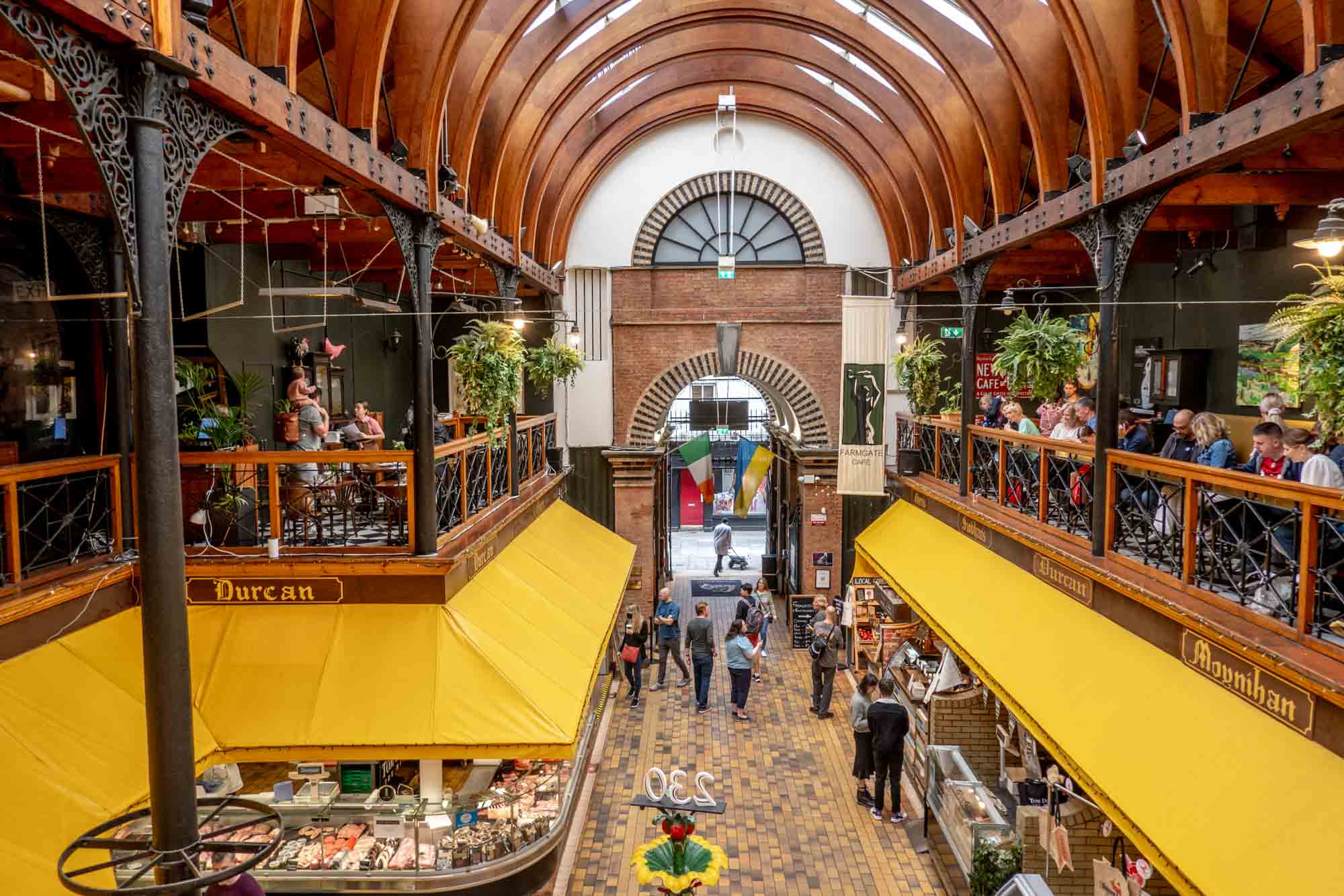 People shopping and eating in a 2-story covered market with yellow awnings