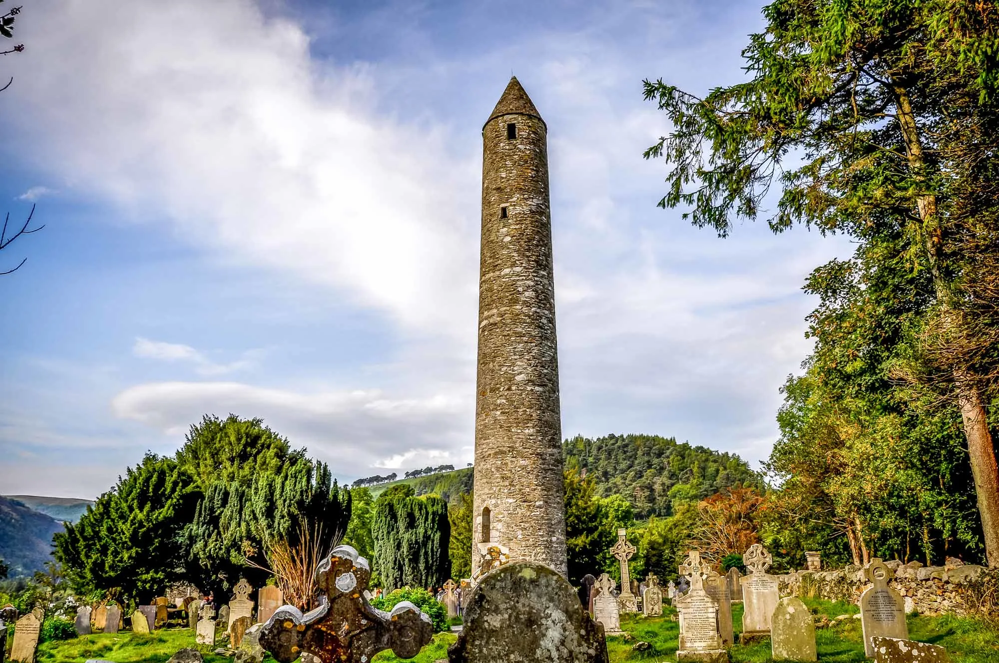 Tall, thin stone tower in an old cemetery set among trees and mountains