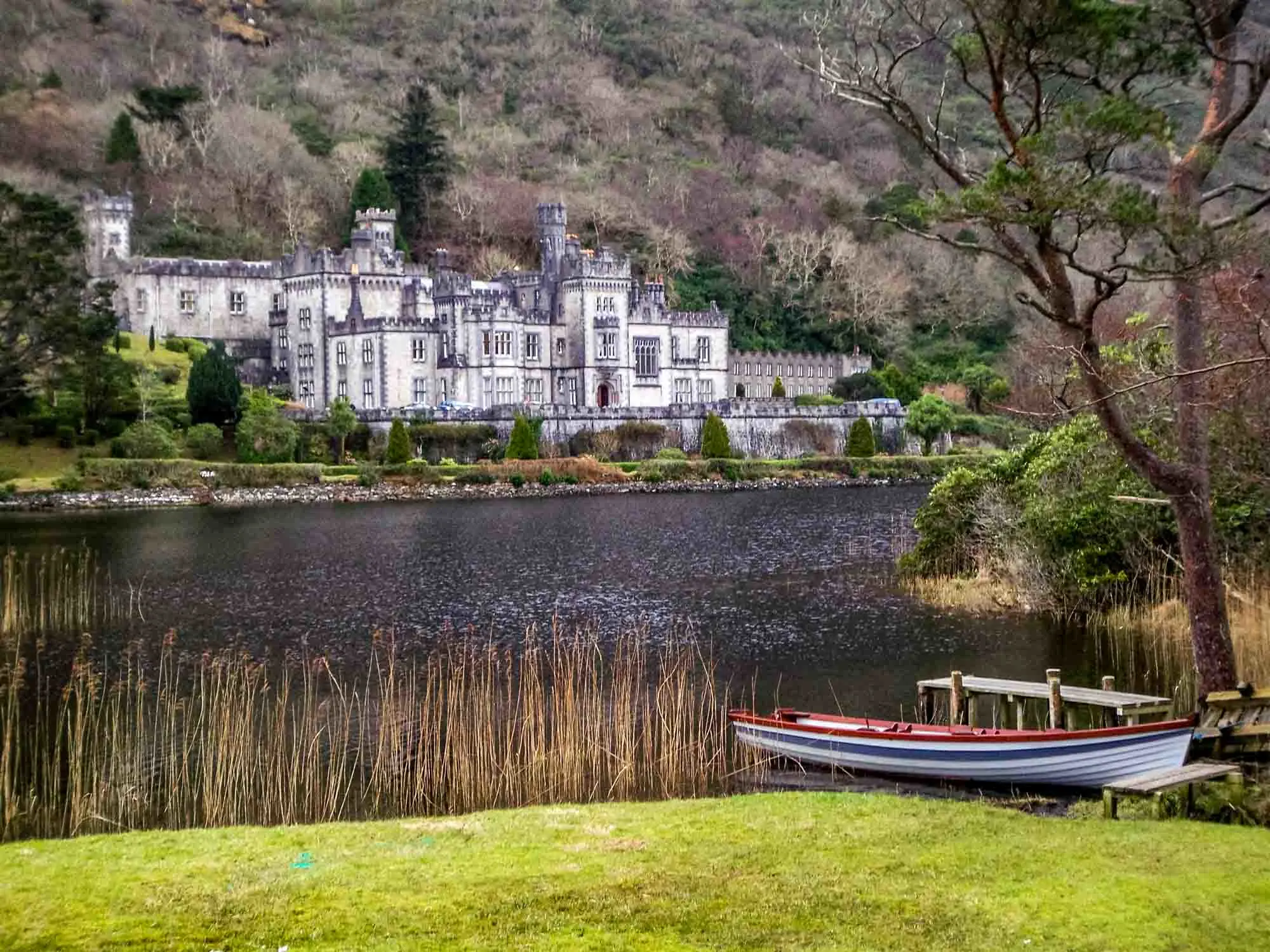 Large mansion at the base of a mountain with a rowboat and lake in the foreground