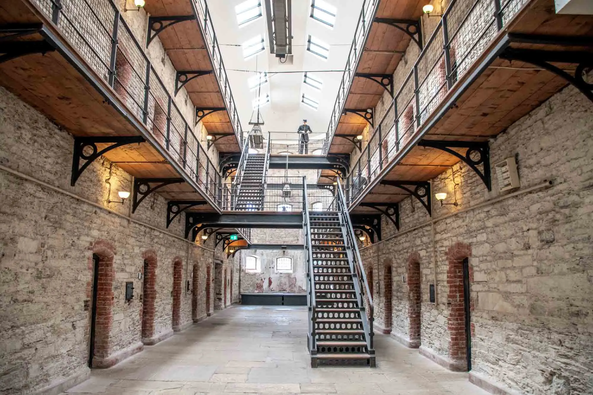 Two-story prison corridor lined with cells and a mannequin representing a warden watching over the area 