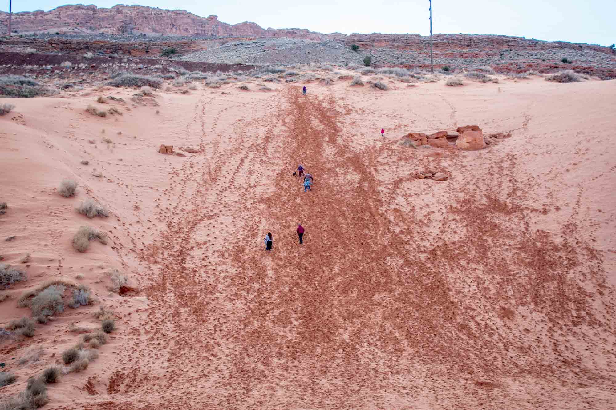 People hiking up the Moab Sand Hill for sledding