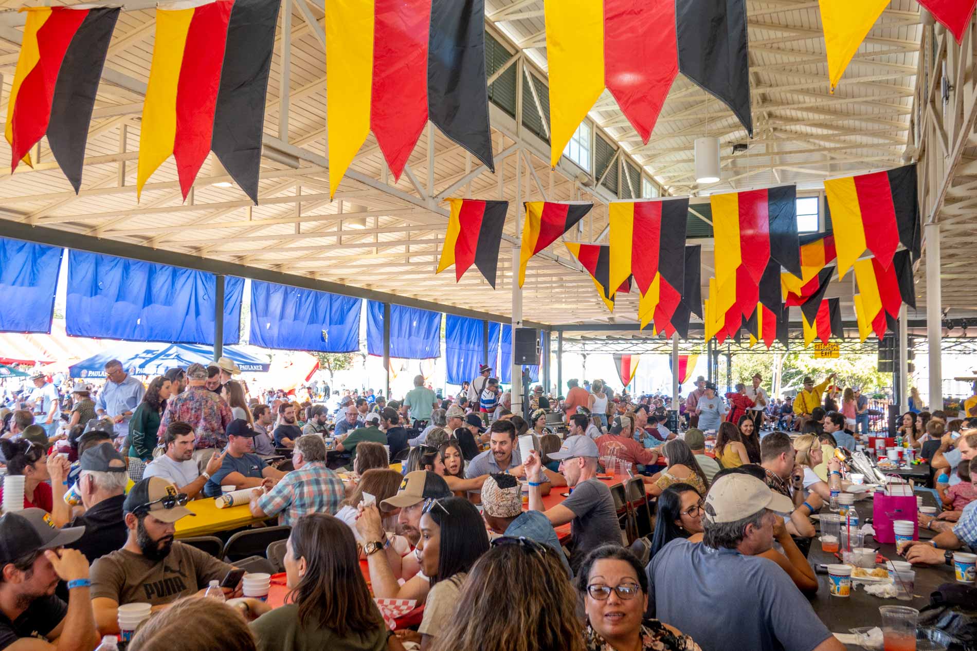 People sitting at tables at a festival tent under a canopy of German flags