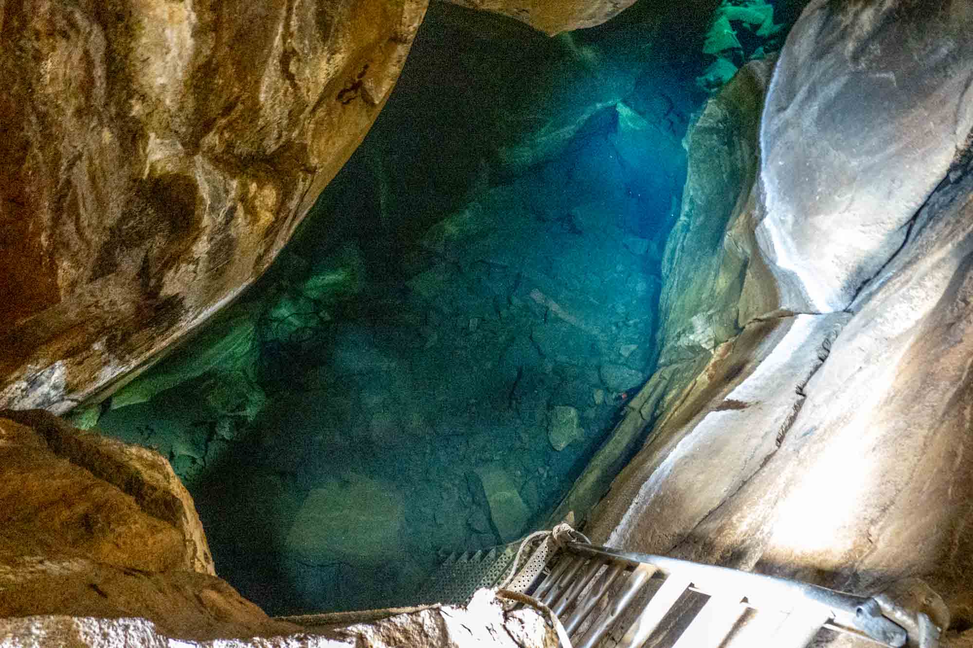 Steel ladder descending in eerie blue waters inside a lava cave