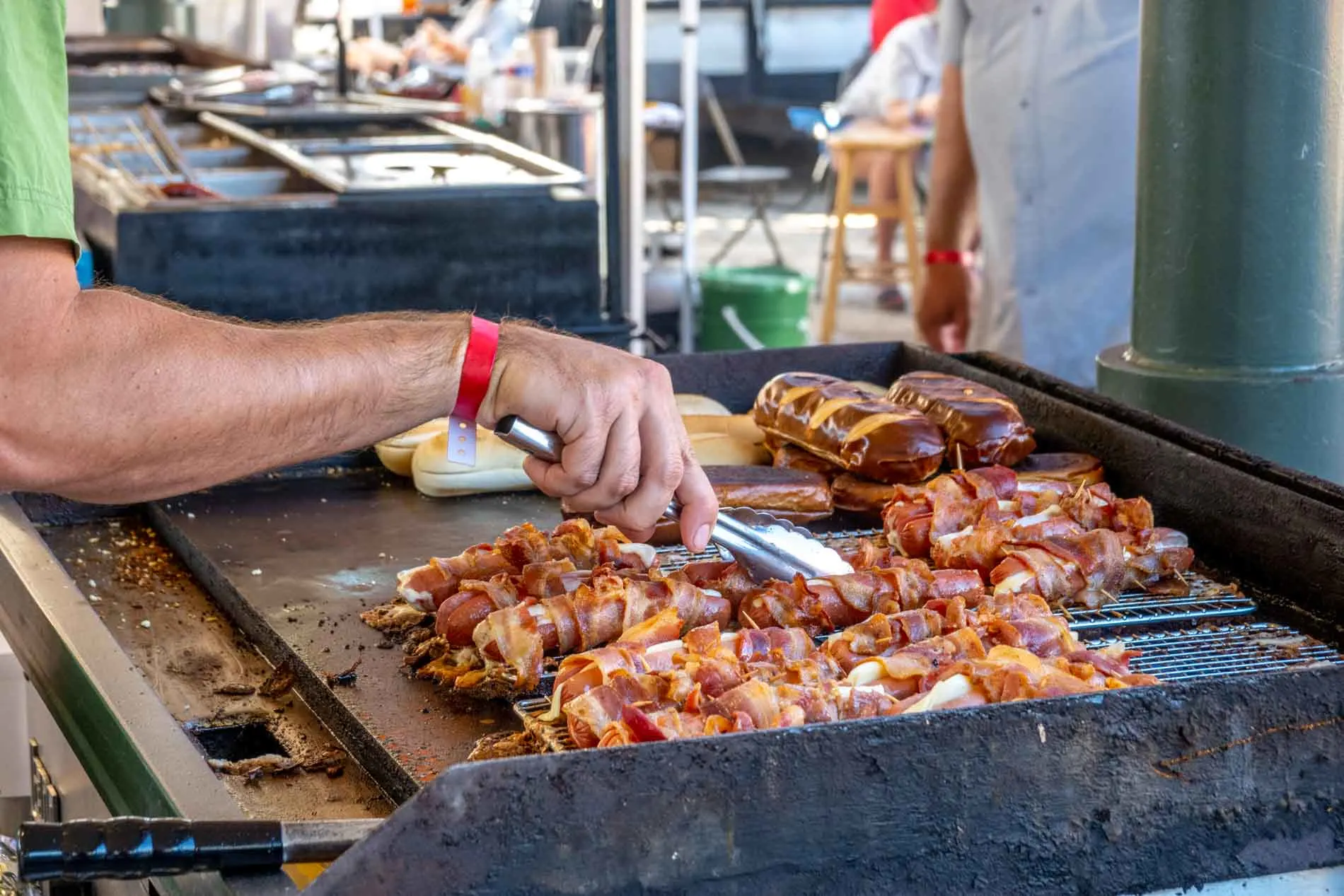 Person cooking bacon-wrapped sausage on a grill