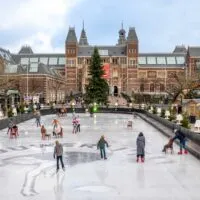 People ice skating in an Amsterdam city square surrounded by Christmas market stalls