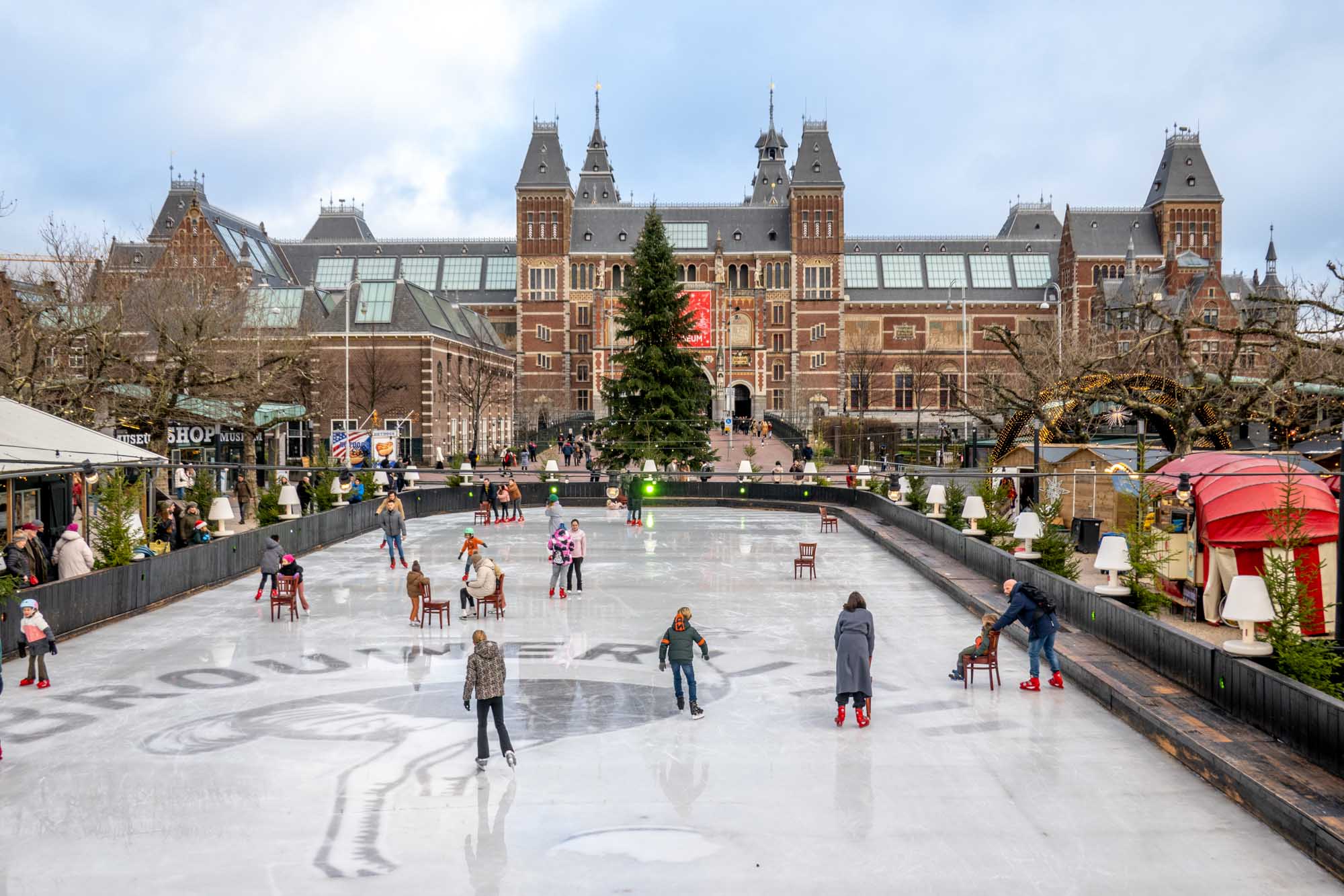People on an ice-skating rink in an Amsterdam city square surrounded by Christmas market stalls