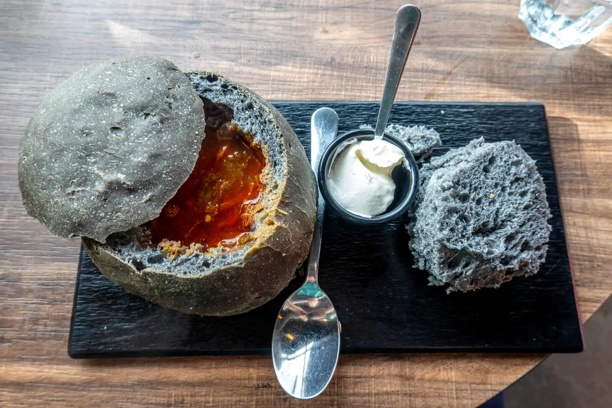 Black bread bowl with soup and sour cream on black slate plate