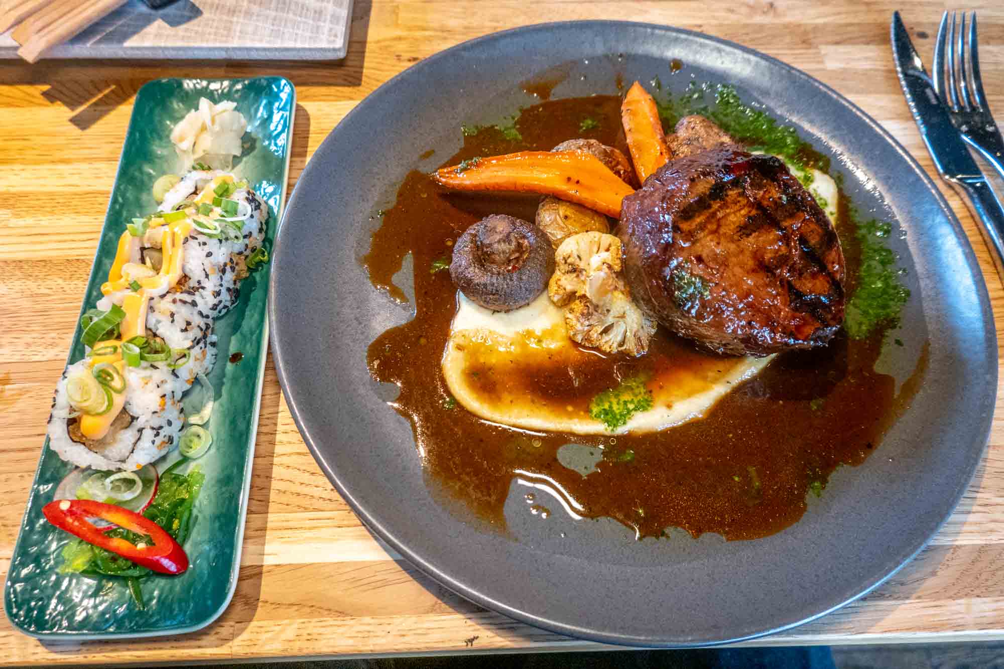Plate of steak with potatoes, carrots and mushrooms, next to small plate of sushi at Rub 23 in Akureyri