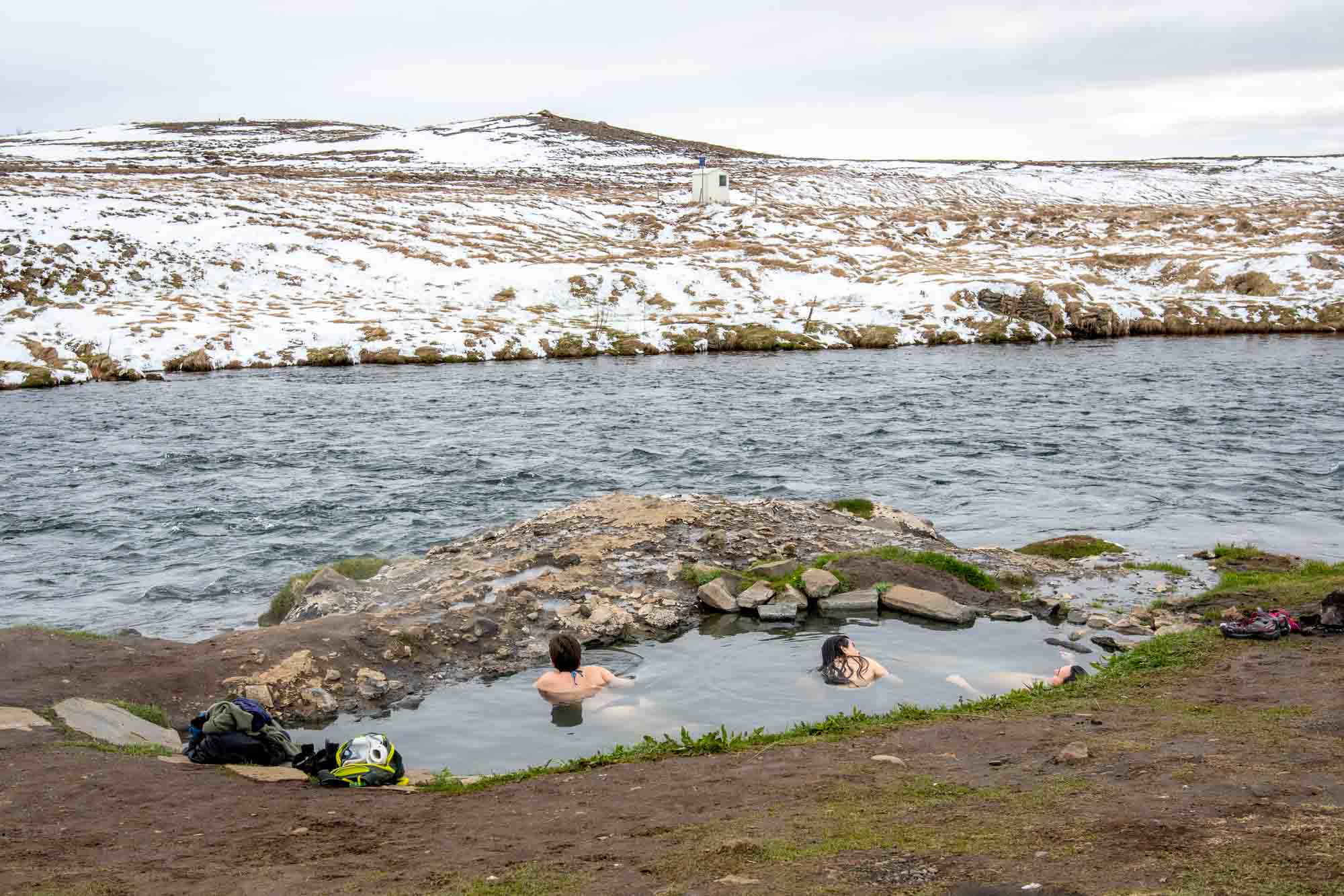 People in a hot springs by a river with snowy hills in the background