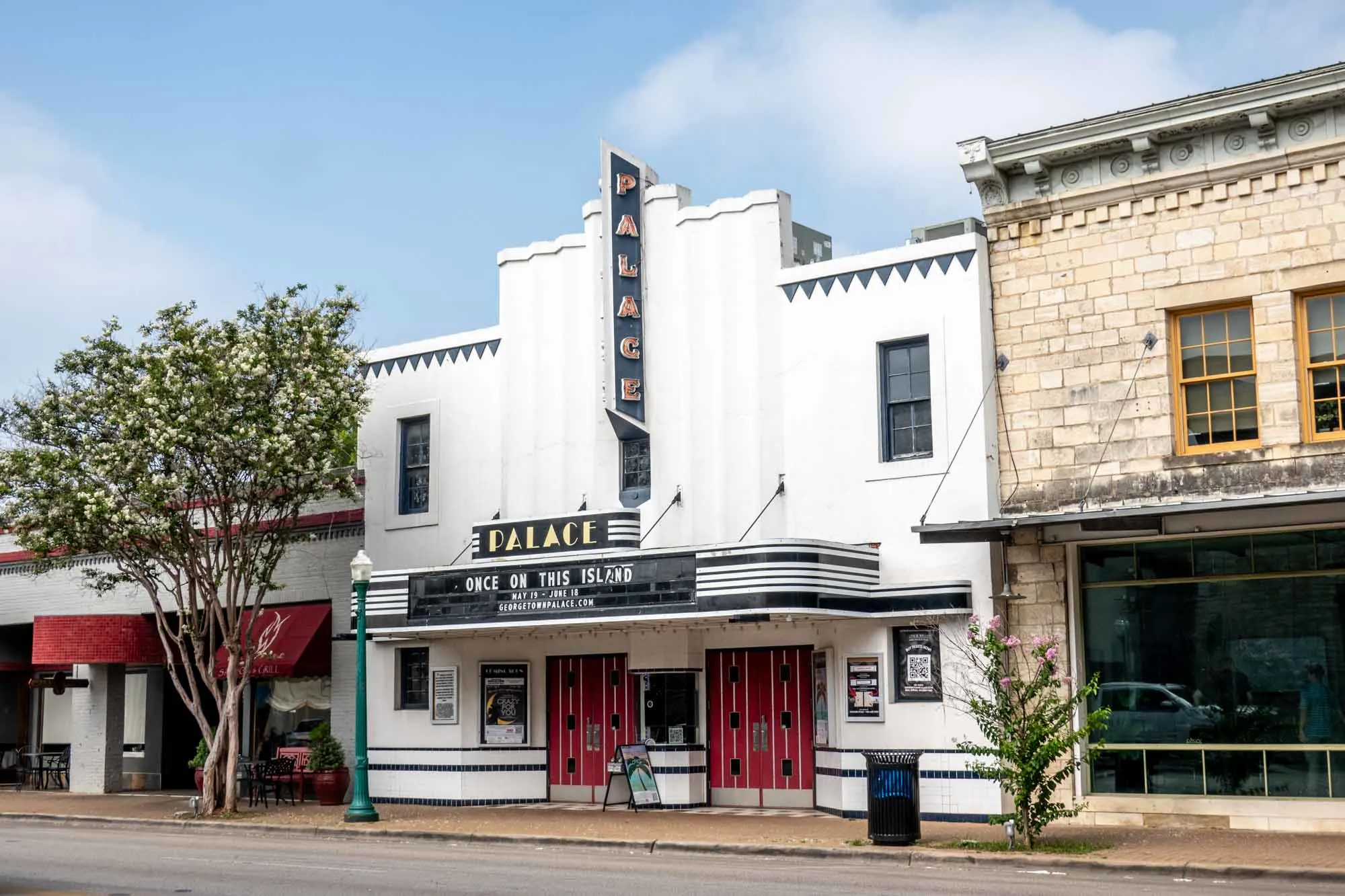 Exterior of a white building with Art Deco decoration, a marguee, and a sign for "Palace"