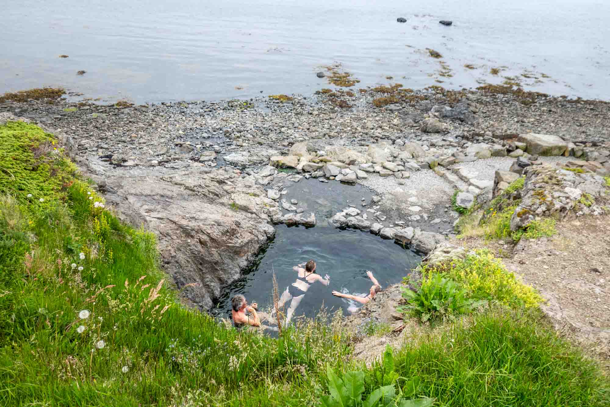 People sitting in hot springs at the edge of the ocean