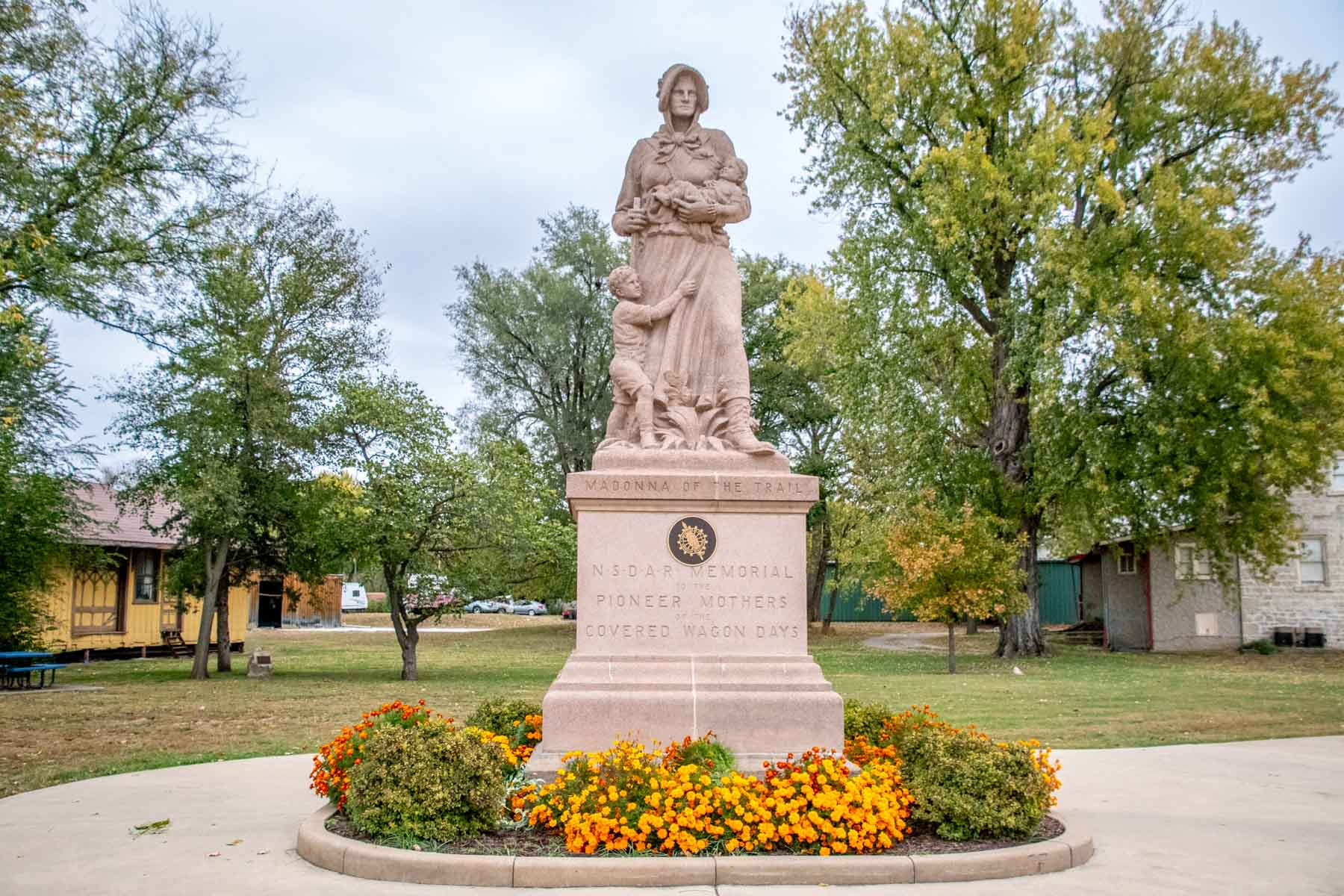 Statue of  woman with two children reading "Madonna of the Trail" and "NSDAR Memorial Pioneer Mothers Covered Wagon Days"