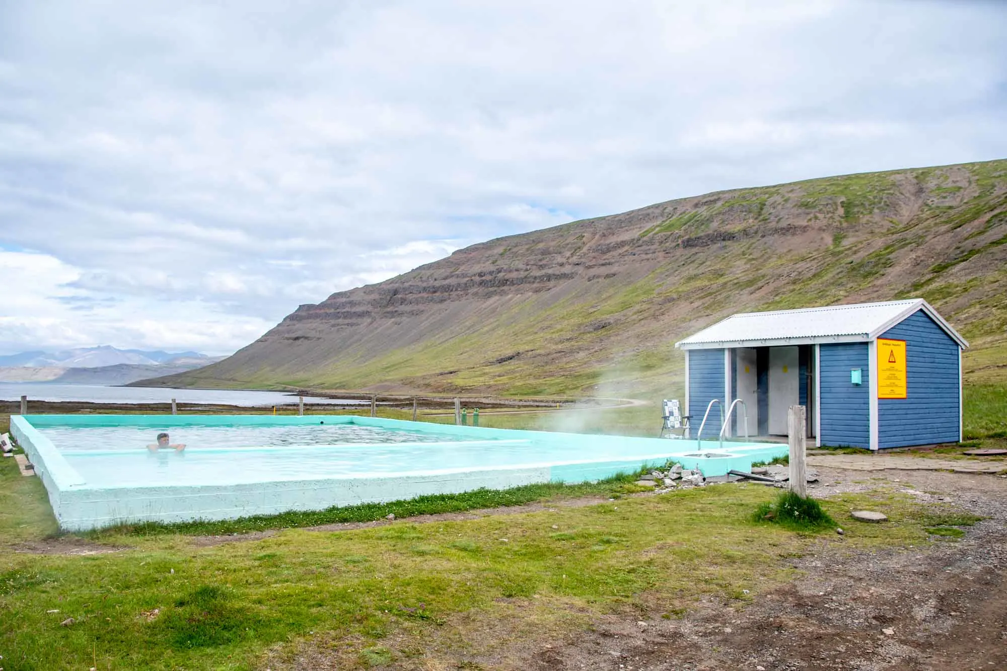 Two green Icelandic hot springs pools next to a blue changing building in the westfjords