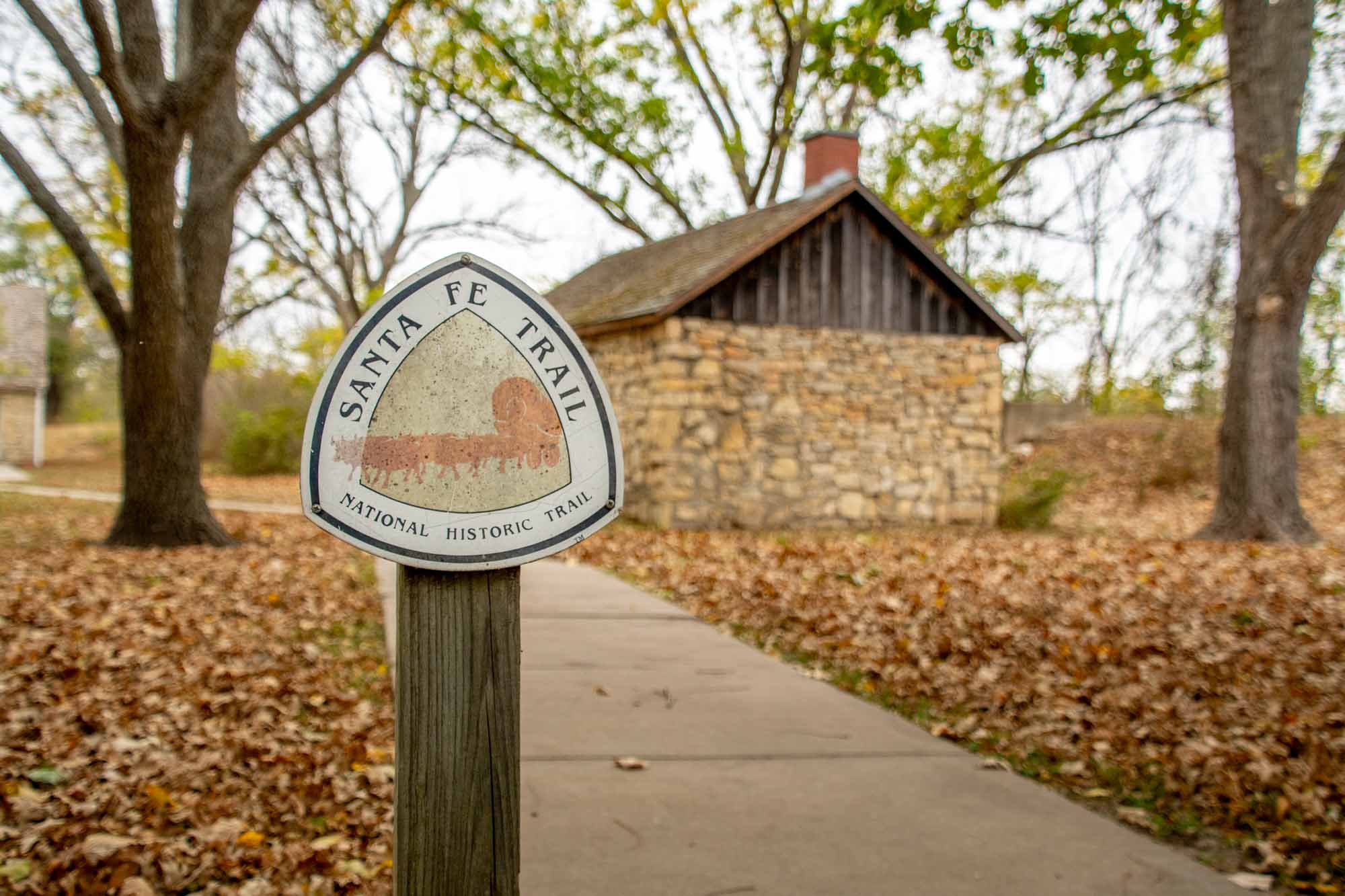 Sign reading "Santa Fe Trail National Historic Trail" in front of  limestone cabin