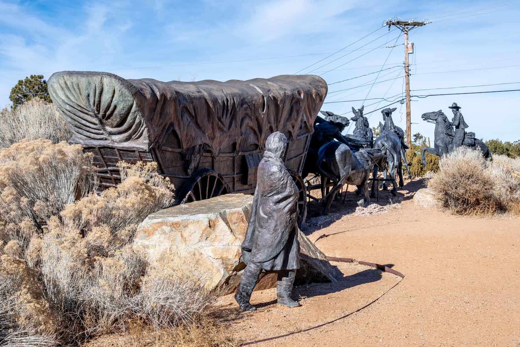 Statue of covered wagon with team of horses and rider on horseback with a woman walking