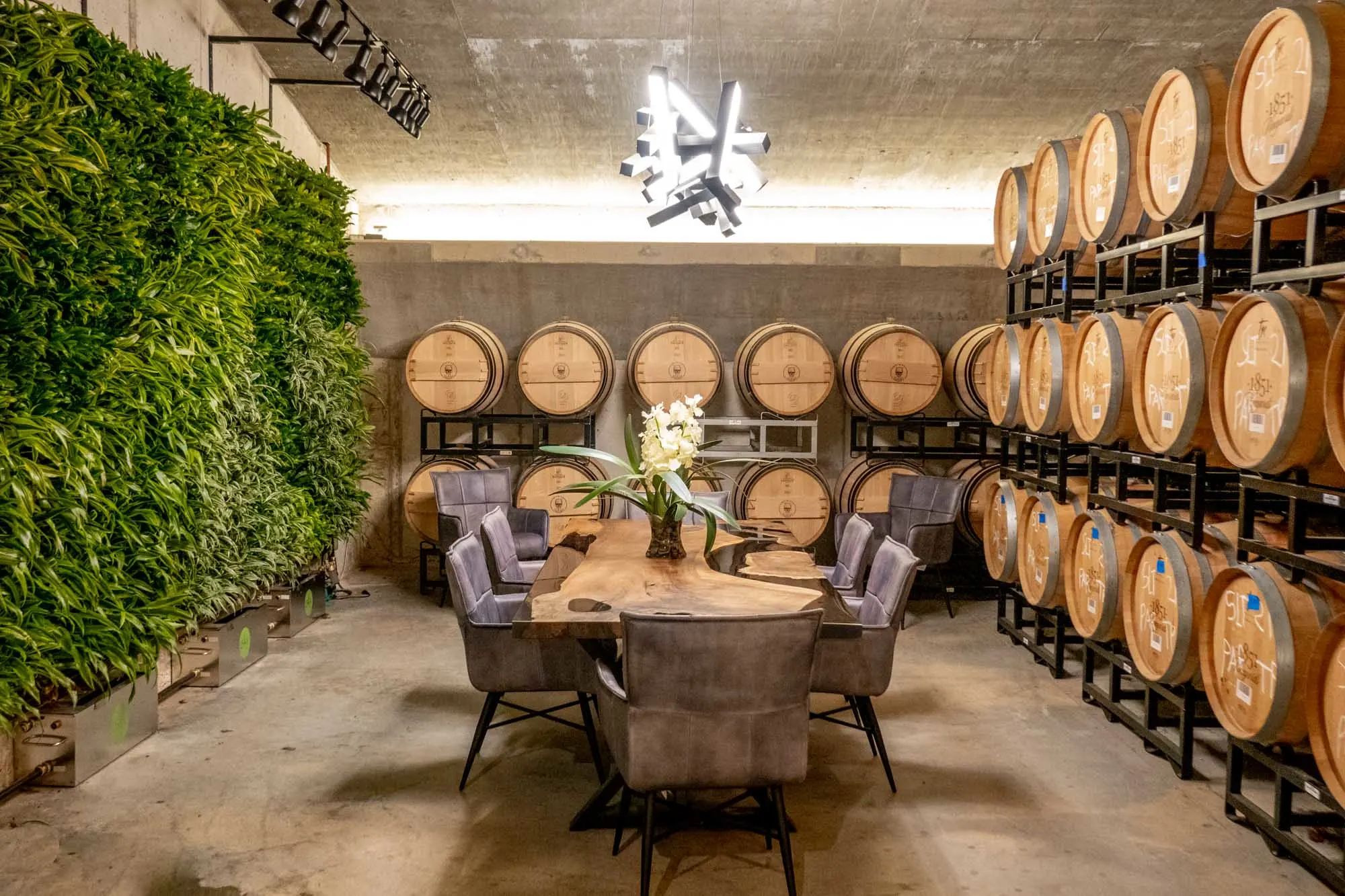 Table in the middle of a room lined with wine barrels and plants