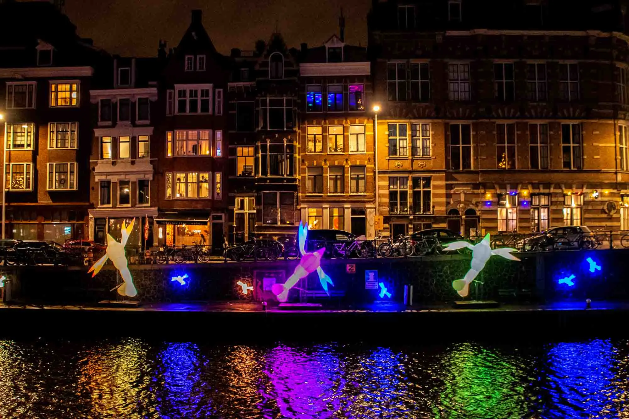 Illuminated artworks along the side of a canal at night.