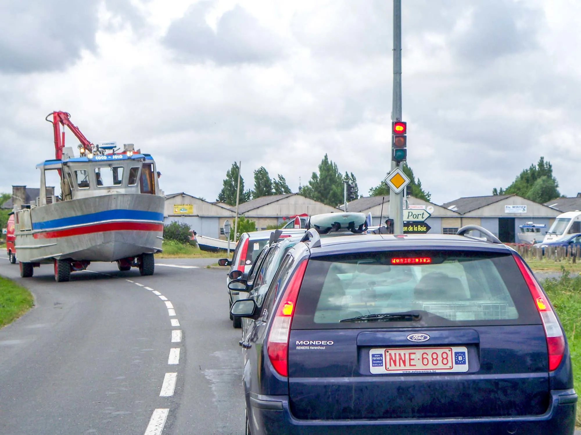 Line of cars at a traffic light yielding to a motorized boat on the road