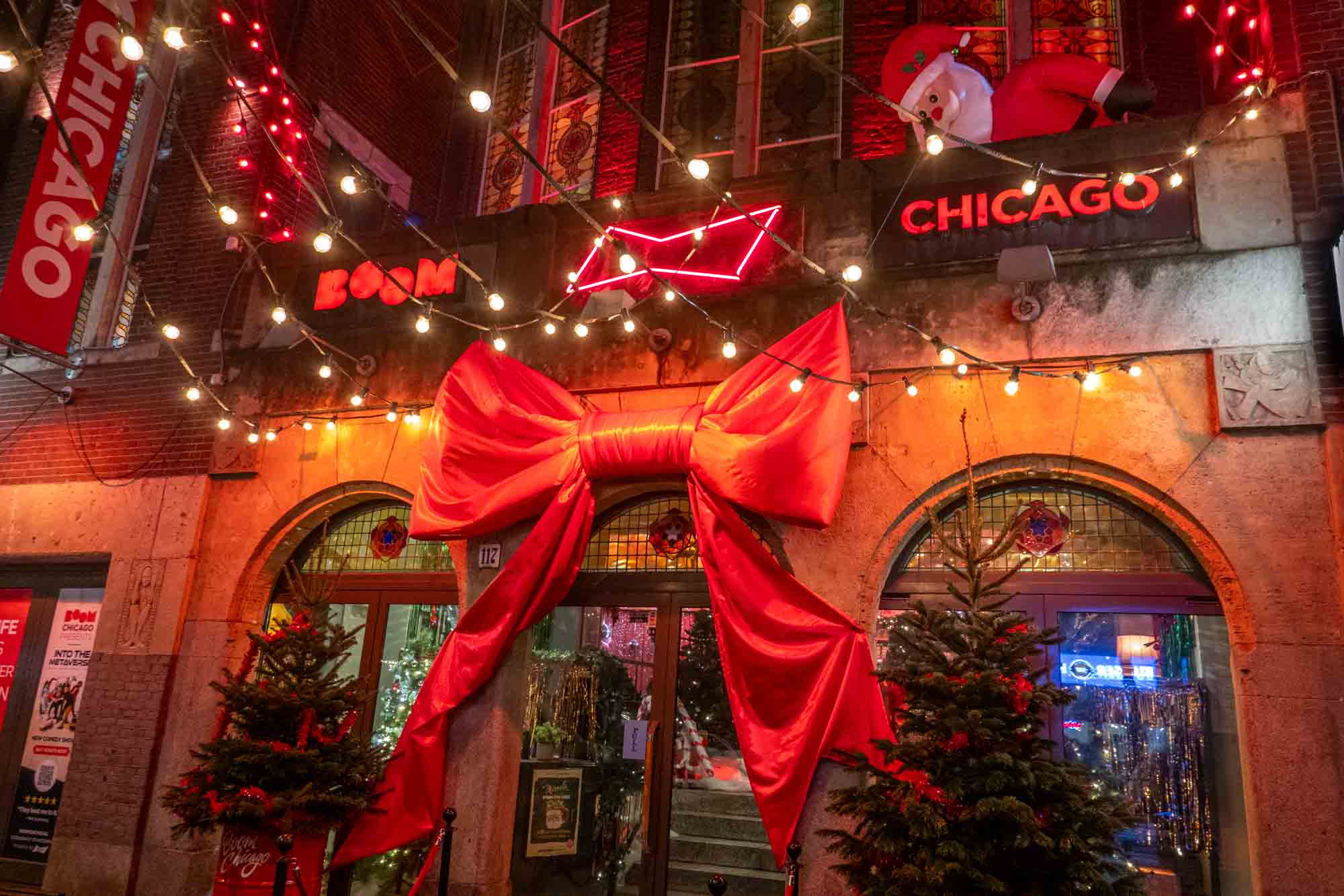 Storefront with a giant red bow and Christmas decorations and a sign for "Boom Chicago."