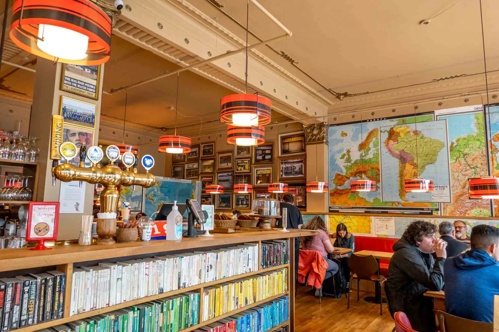 Interior of fun cafe with maps on the walls and a bookcase for a bar