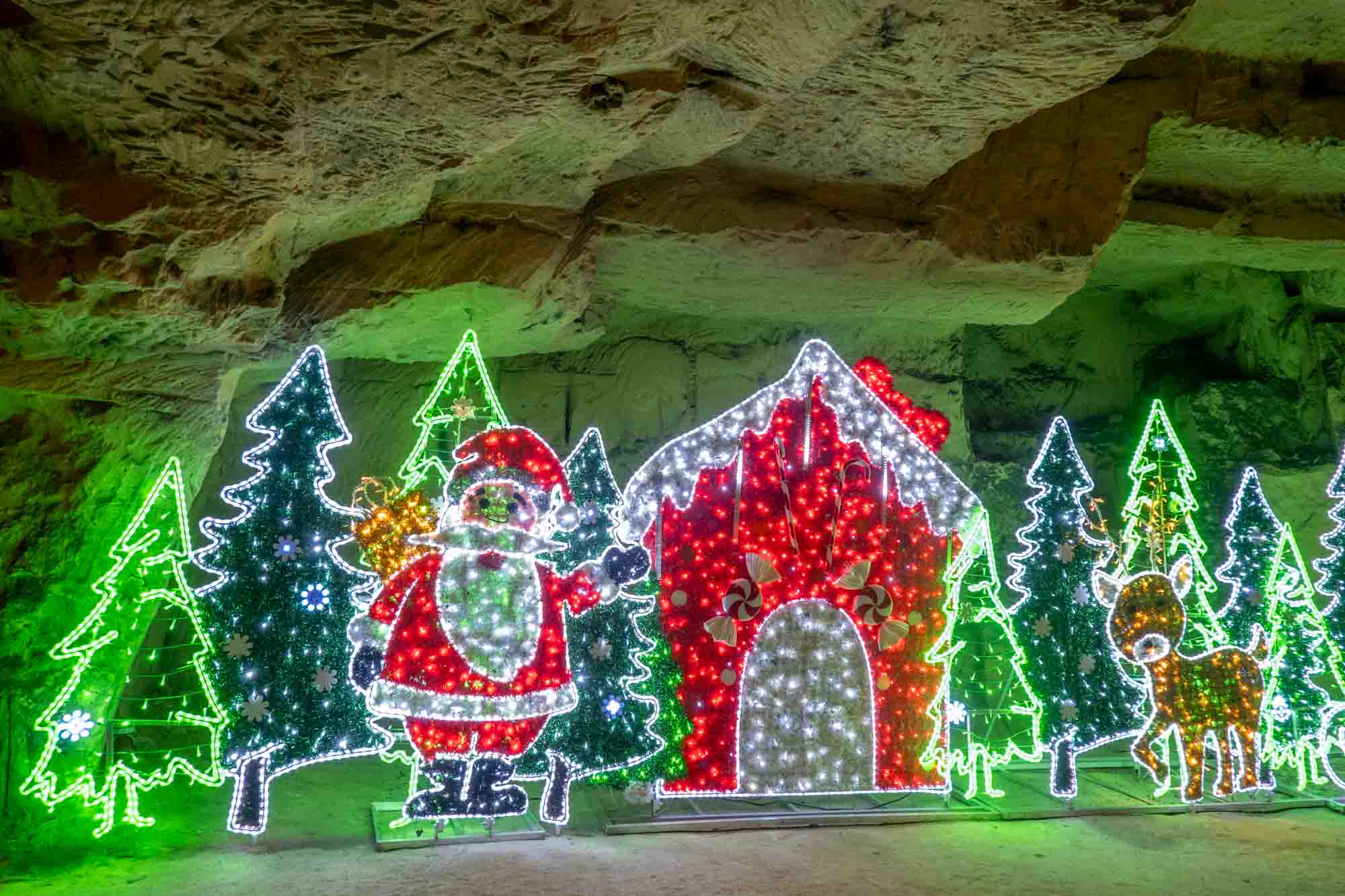Christmas light display in a cave including Santa and Christmas trees.