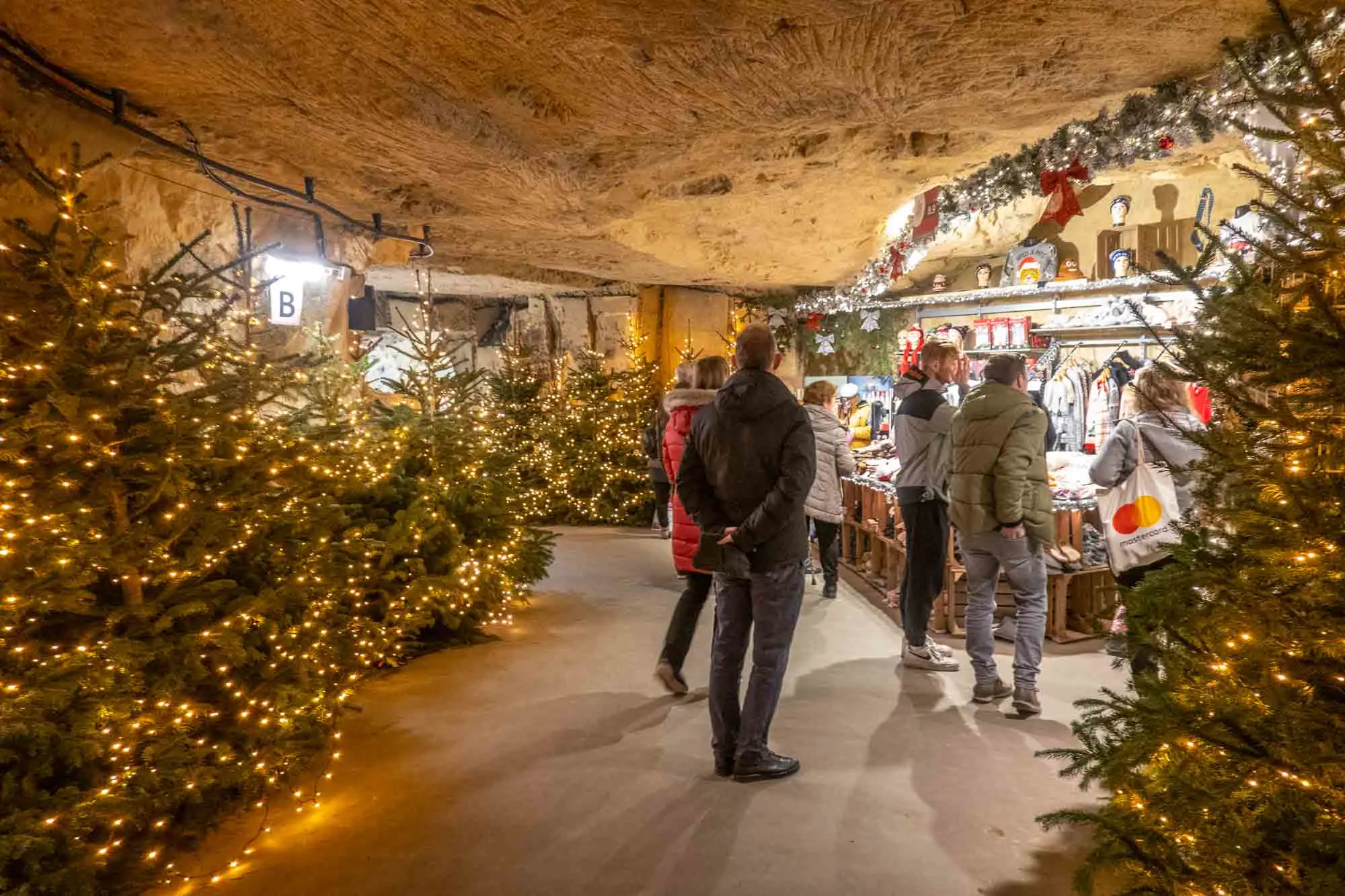 Shoppers at the Valkenburg Christmas market in a tunnel lined with Christmas trees.