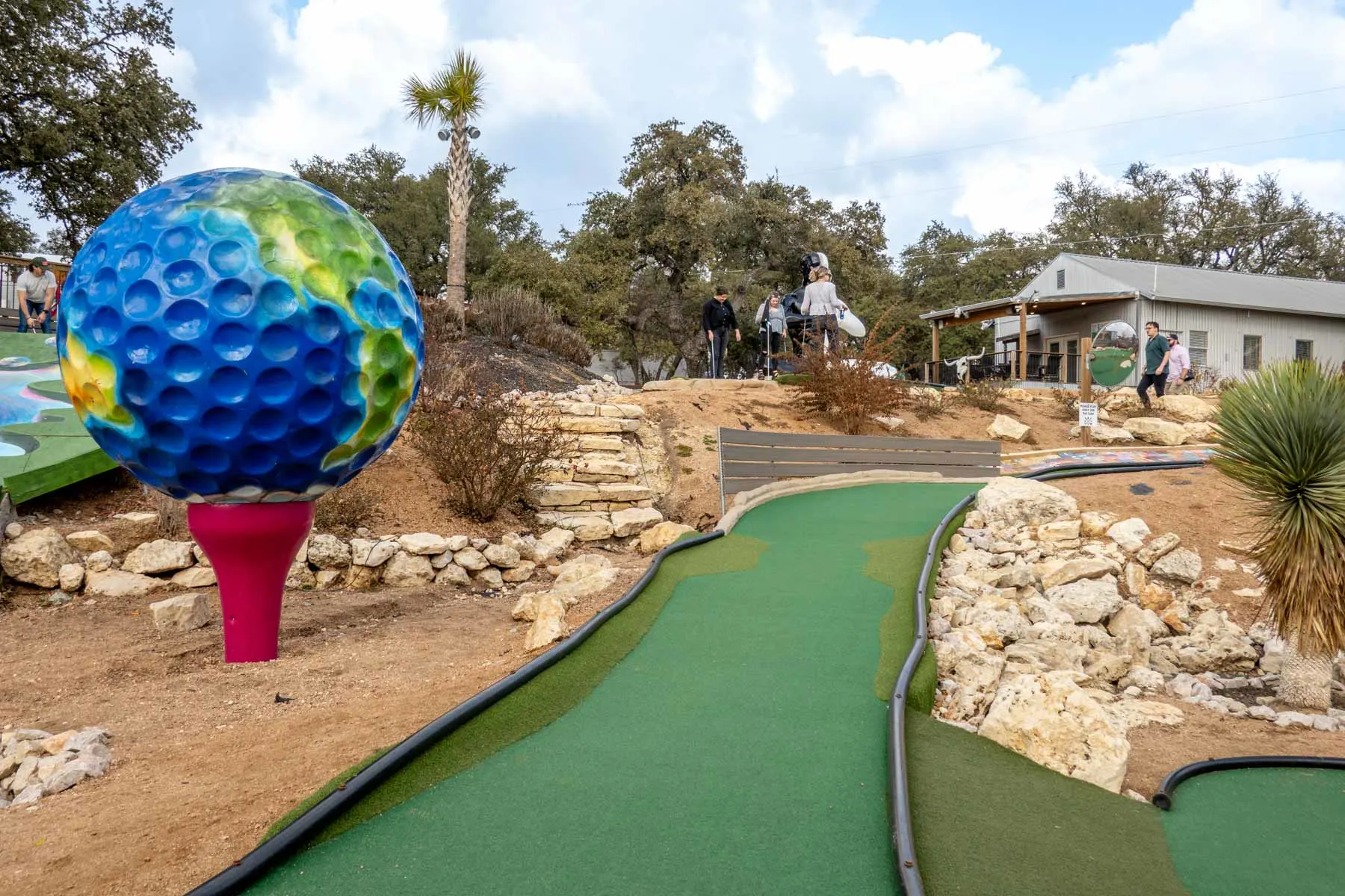Giant golfball painted like a globe on a giant tee next to a mini-golf hole. 