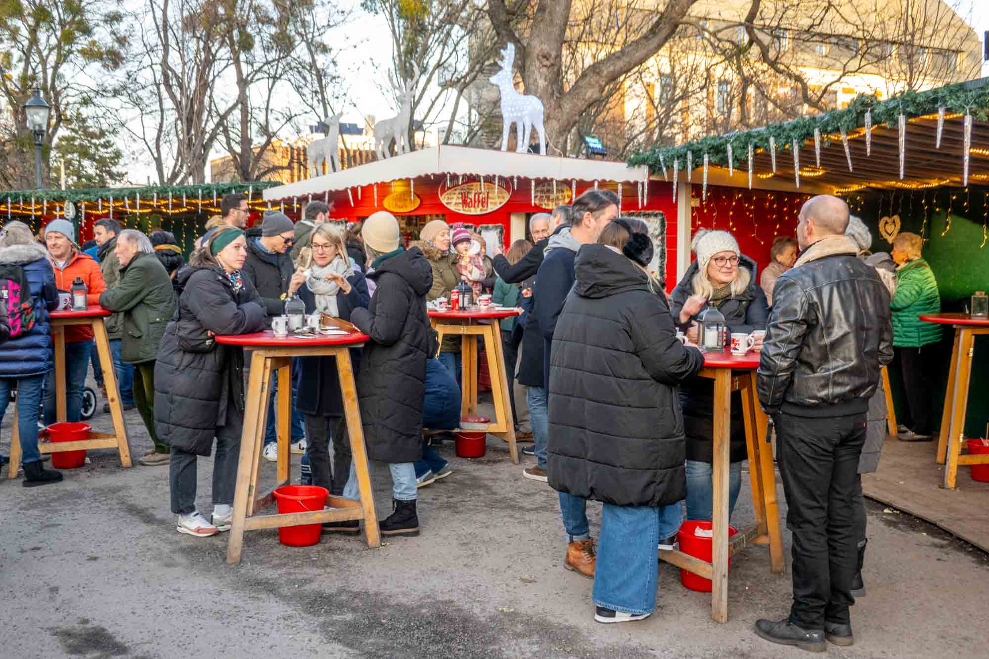 People standing at tables at a food vendor decorated with icicles and garland.