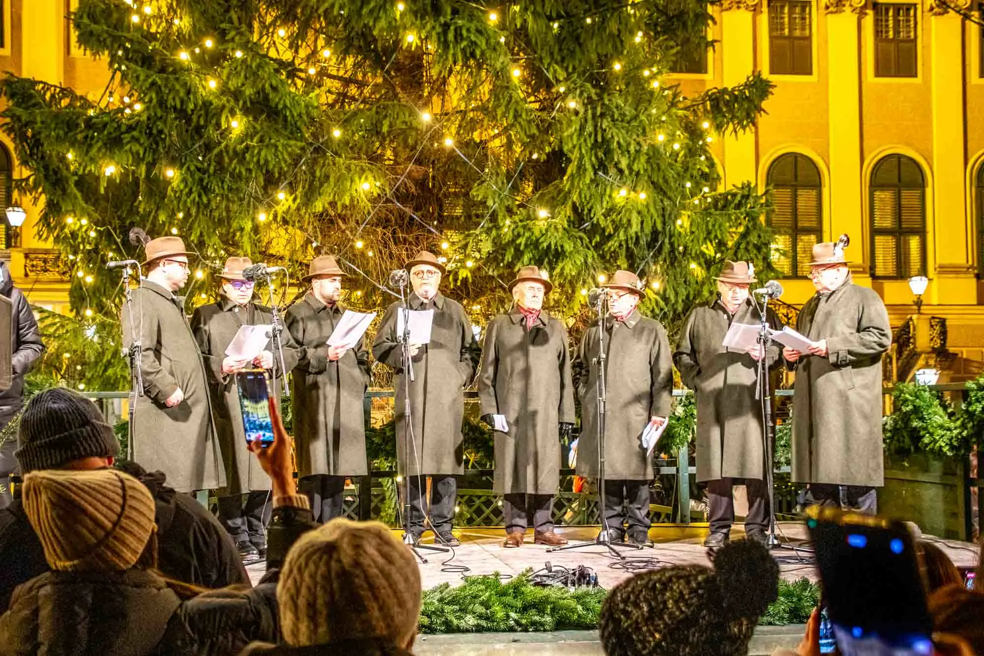 Men's choir performing on stage in front of a Christmas tree.