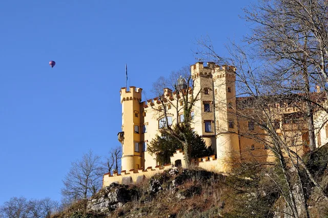 Yellow exterior of Hohenschwangau Castle with hot air balloon in the sky